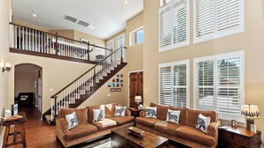 A spacious living room with a large brown sectional sofa, a wooden coffee table, and a staircase leading to an upper level. - High Timber Family Retreat: Luxury Family Fun in High Timber Ranch! Spacious Fenced Yard! Game Room! (Big Bear City)