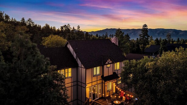 Ein zweistöckiges Haus mit Balkon, umgeben von Bäumen und Bergen im Hintergrund.