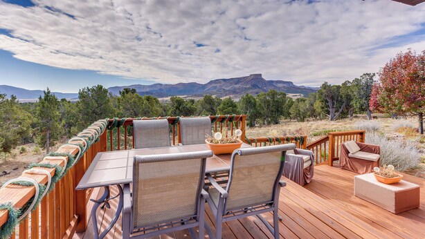 A wooden deck with outdoor furniture, including a table and chairs, overlooking a scenic landscape with mountains and trees. - Scenic Mancos Hideaway < 2 Mi to Mesa Verde! (Mancos)