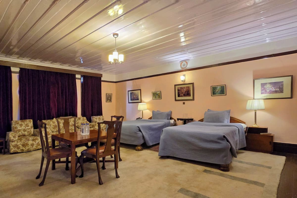 Ein Hotelzimmer mit zwei Betten, einem Esstisch mit Stühlen, einer Kristallleuchtre und gerahmten Bildern an den Wänden.