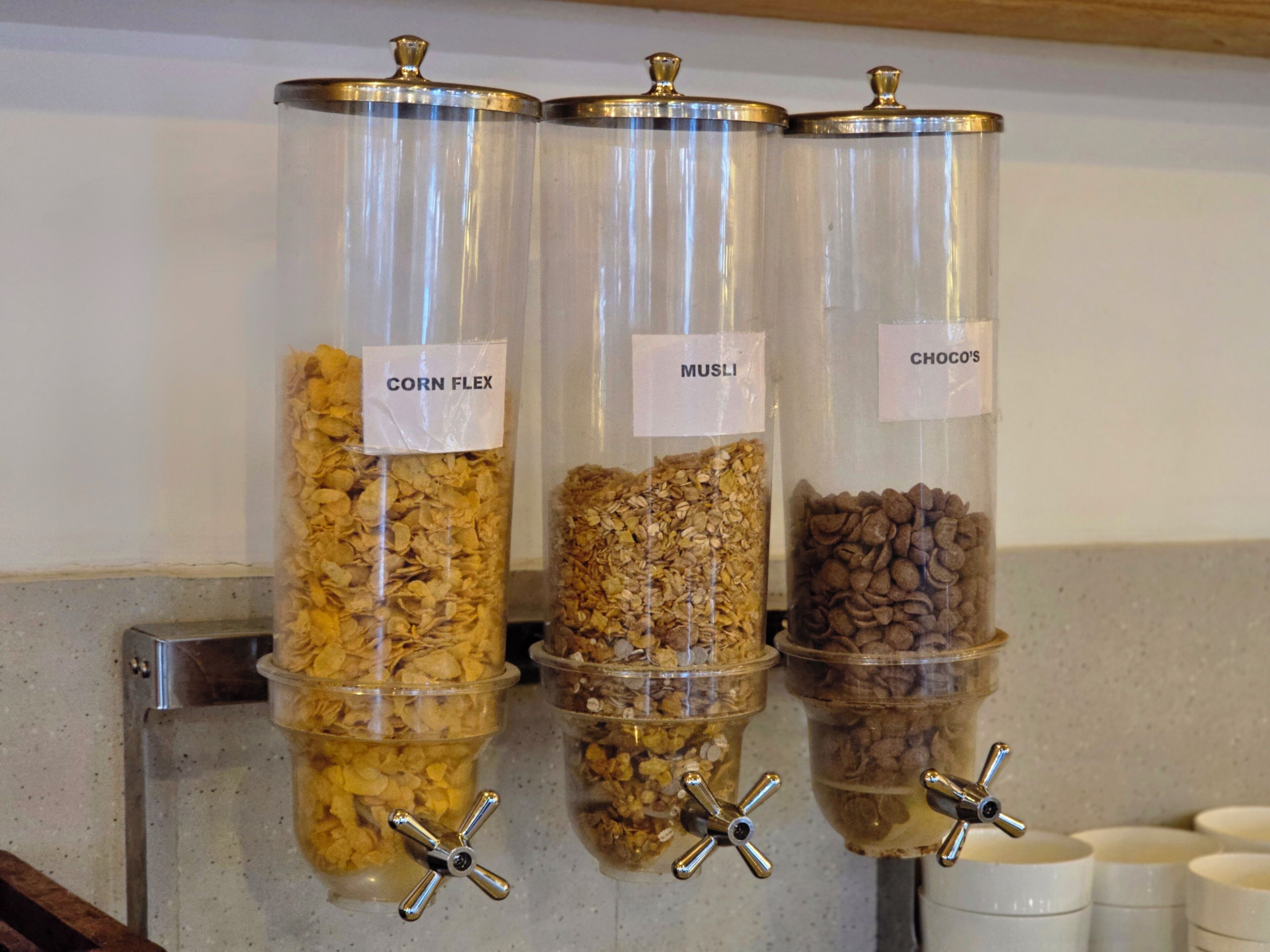 Three transparent containers with labels for 'CORN FLEX,' 'MUSLI,' and 'CHOCO'S' on a countertop.