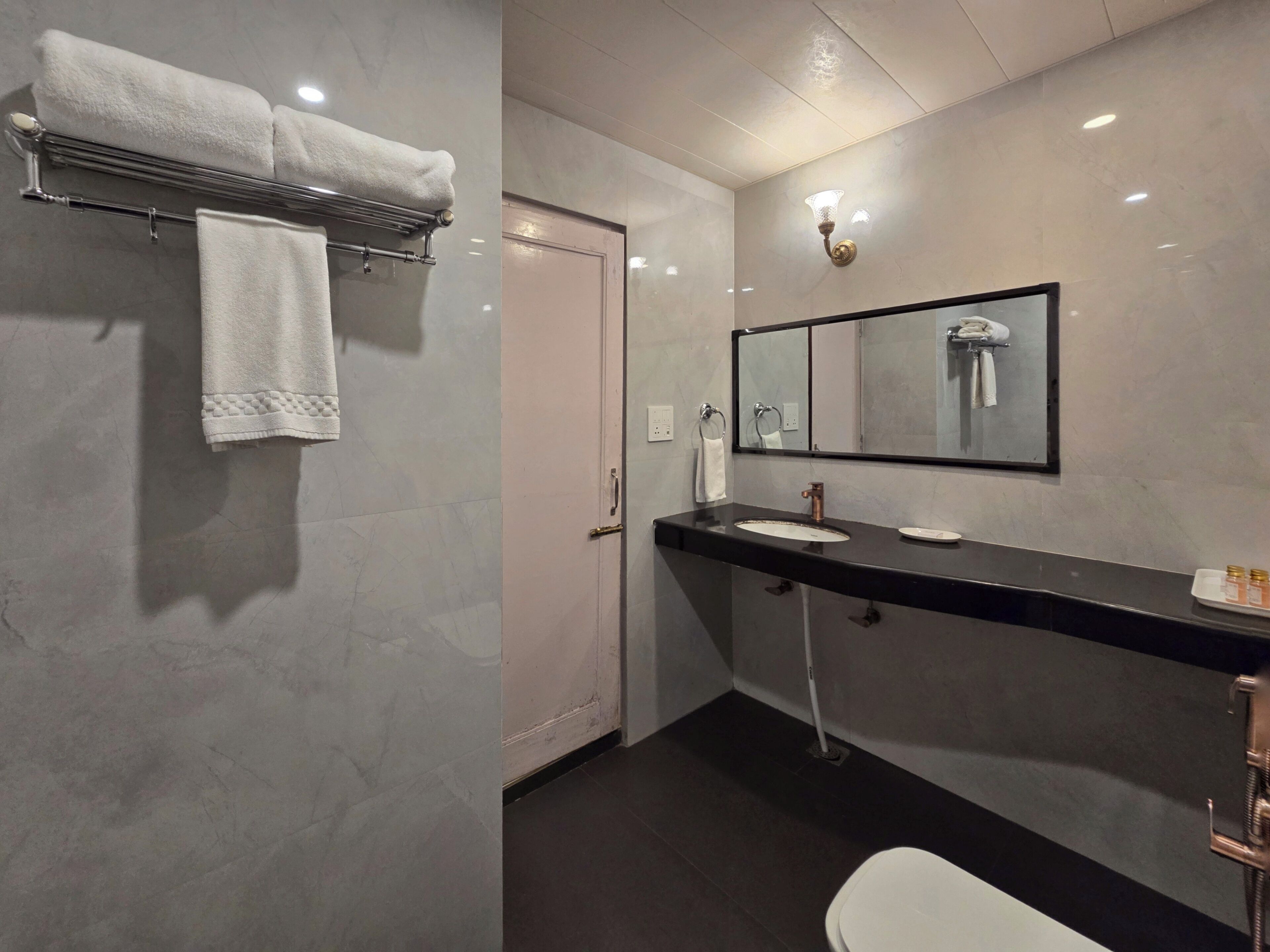 A modern bathroom with a marble wall, a black countertop, a sink, a mirror, and a toilet.