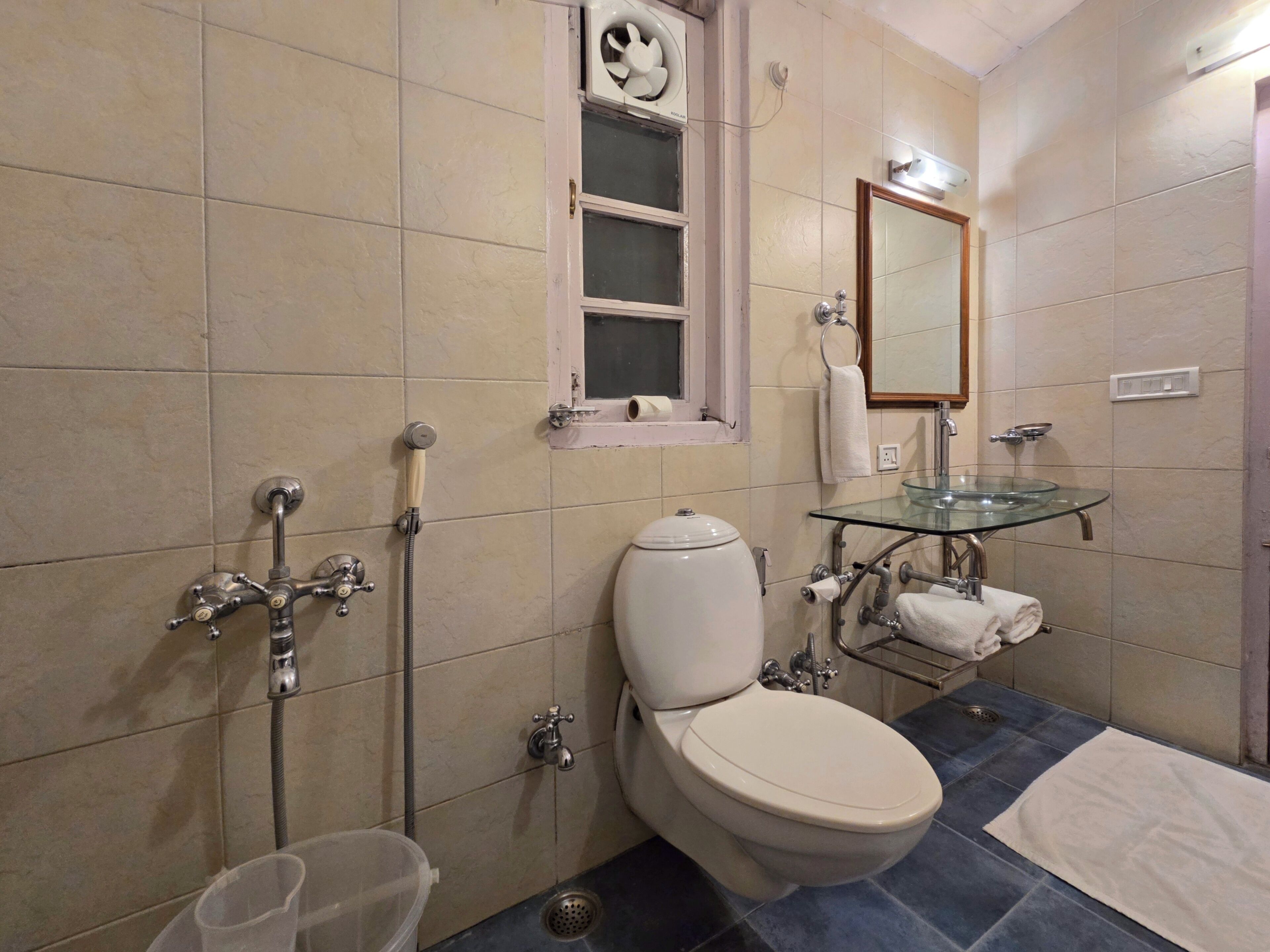A bathroom with a toilet, a glass sink, a shower, and a window.