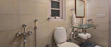 A bathroom with a toilet, a glass sink, a shower, and a window.