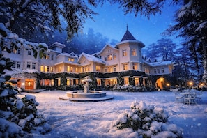 A large, multi-story hotel with a central courtyard, surrounded by snow-covered trees and a fountain. - Woodville Palace Shimla Heritage (Shimla)