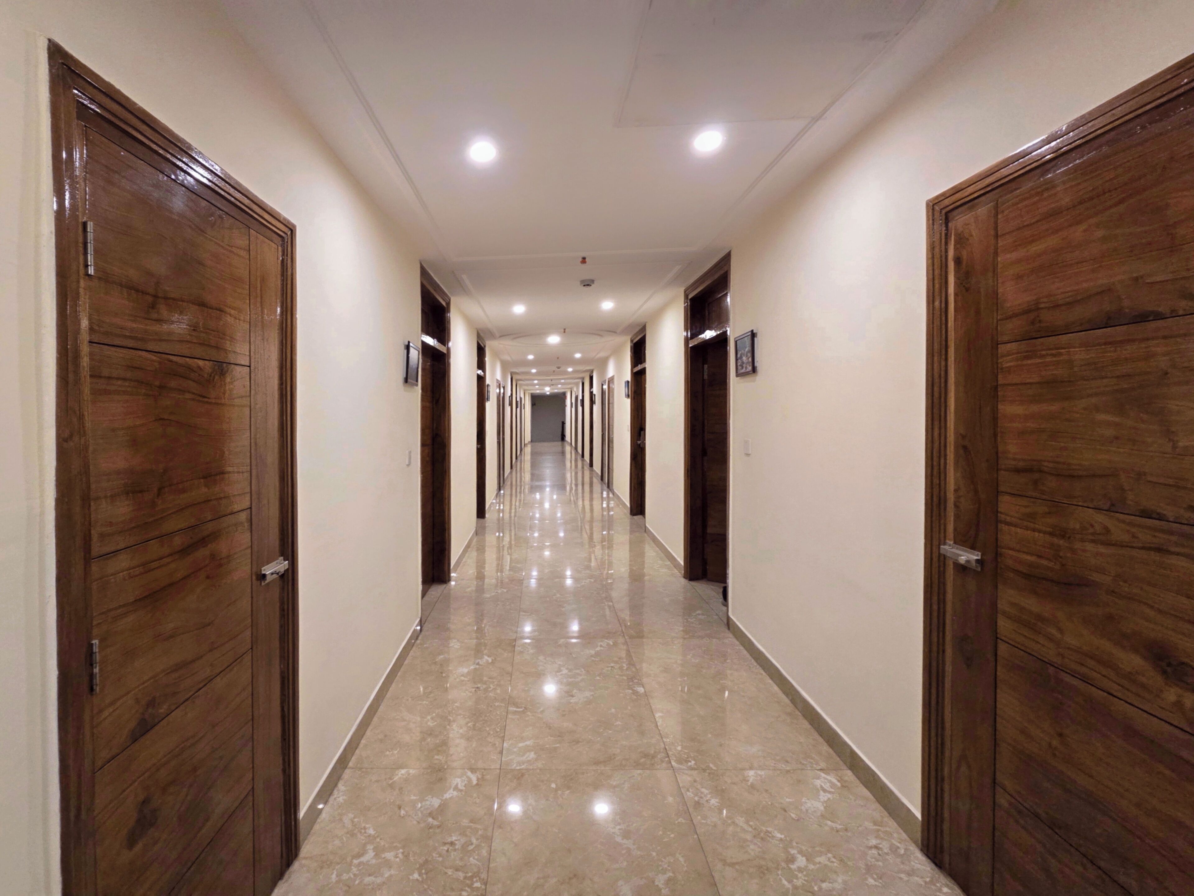 A long, well-lit hallway with wooden doors on both sides and a shiny tiled floor.