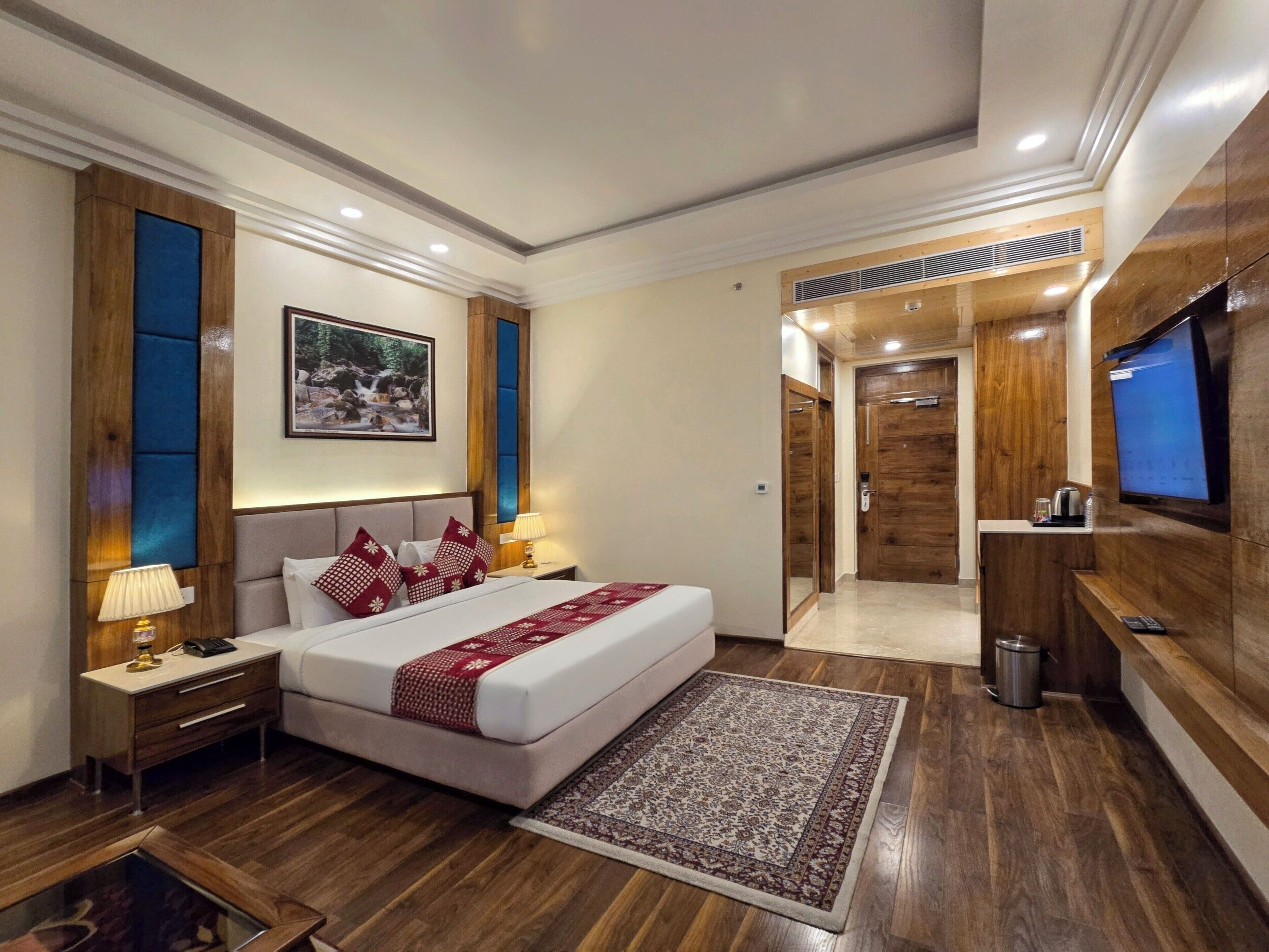 A modern hotel room with a large bed, bedside tables, a TV, and a wooden wardrobe.