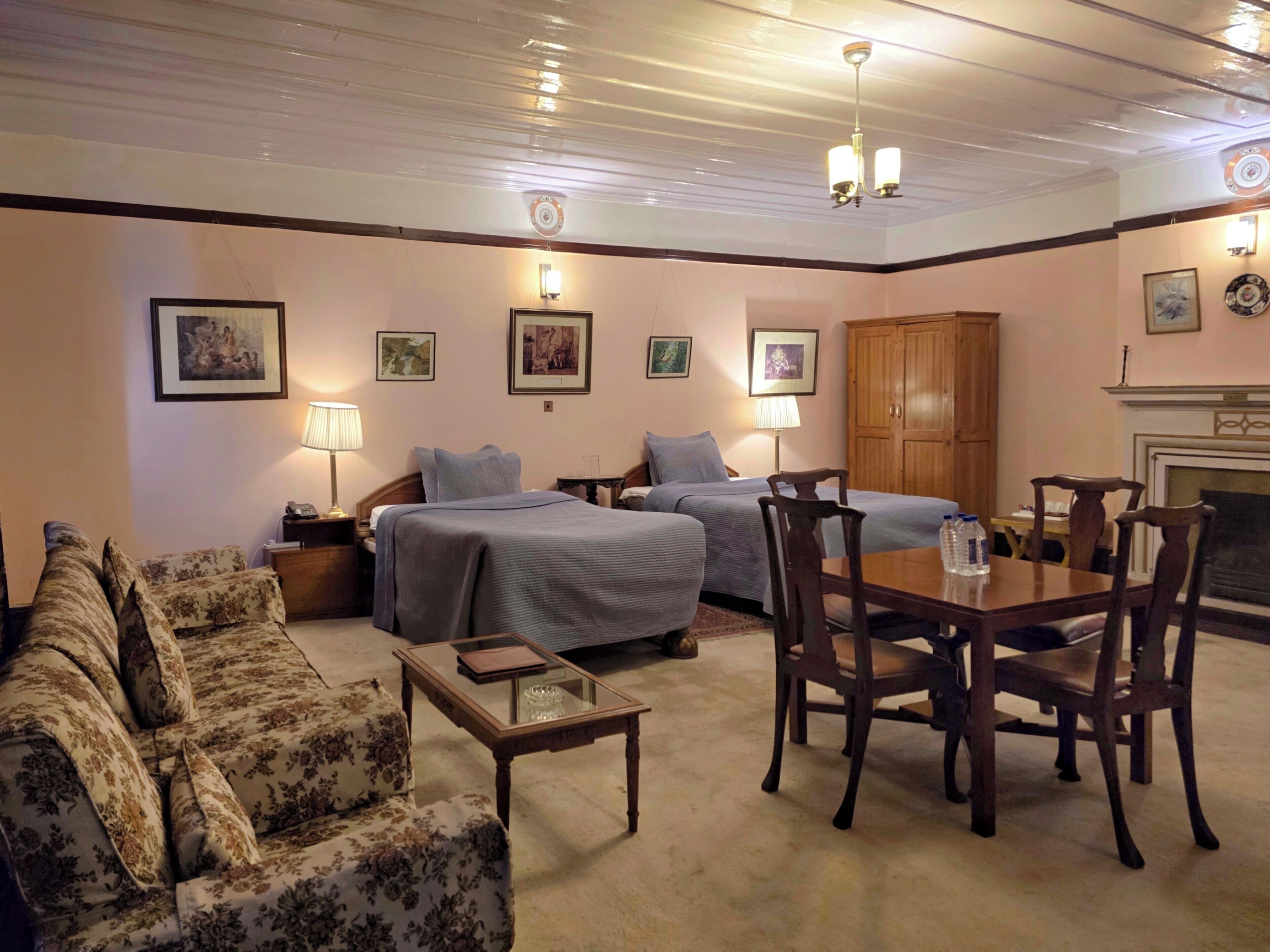 Una habitación de hotel con dos camas, un sofá, una mesa de comedor con sillas y una chimenea.