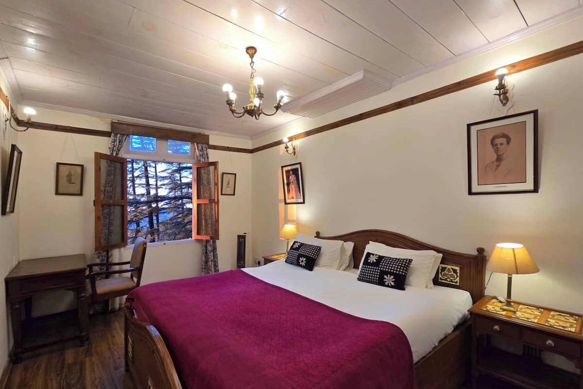 Ein Schlafzimmer mit einem großen Bett, einem hölzernen Kopfteil, einem Nachttisch mit Lampe, einem Schreibtisch mit Stuhl und einem Fenster mit Vorhängen.