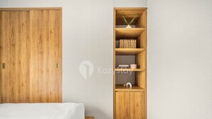 A bedroom with a wooden wardrobe, a built-in wooden shelf unit, and a bed with white bedding. - AKASA by Kozystay (Jakarta)