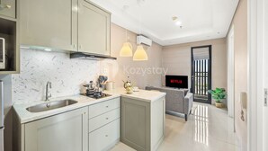 A modern kitchen with a built-in sink, cabinets, and a countertop. There is a television mounted on the wall and a plant on the floor. - AKASA by Kozystay (Jakarta)