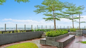 A rooftop garden with concrete planters, a wooden deck, and a view of the city skyline. - AKASA by Kozystay (Jakarta)