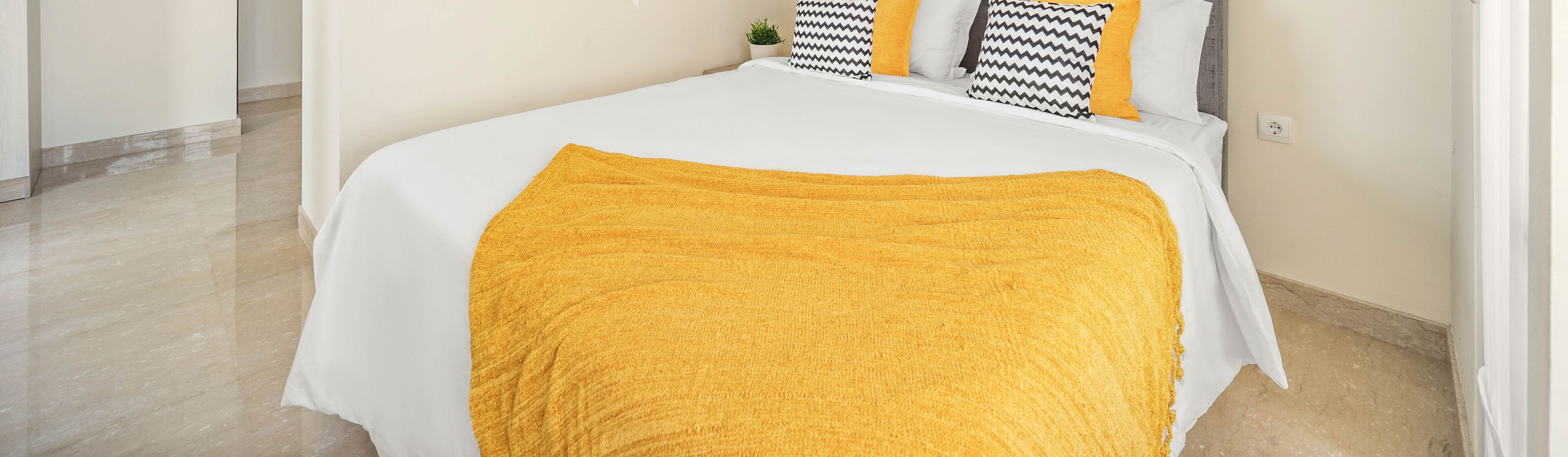 Un letto rifatto con un piumone bianco e una coperta gialla.