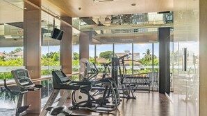 A gym with cardio machines, weight equipment, and large windows offering a view of greenery and buildings. - SOLEIL by Kozystay (Jakarta)