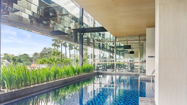 A modern indoor swimming pool with glass walls, surrounded by greenery and a view of the city. - SOLEIL by Kozystay (Jakarta)