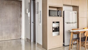 A modern kitchen with a built-in microwave, refrigerator, and water dispenser. There is a dining area with a table and chairs. - SOLEIL by Kozystay (Jakarta)