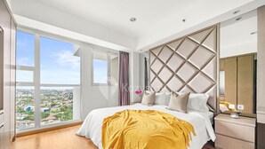 A modern bedroom with a large bed, a nightstand, a mirror, and a view of the city through large windows. - SOLEIL by Kozystay (Jakarta)