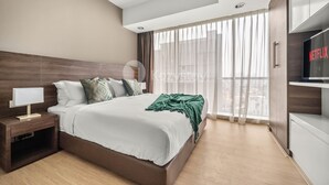 Un dormitorio moderno con una cama grande, una mesita de noche, un televisor y vistas de la ciudad a través de cortinas translúcidas.