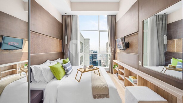 Een moderne hotelkamer met een groot bed, een televisie, een bureau met dienblad, en een groot raam met uitzicht op de stad.