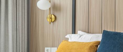Una habitación de hotel con cama, mesita de noche, lámpara y cortina.