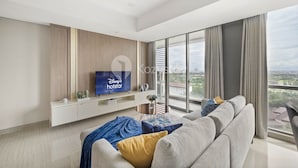 A modern living room with a large flat-screen TV, a sofa, and a large window offering a city view. - VUE by Kozystay (Curug)