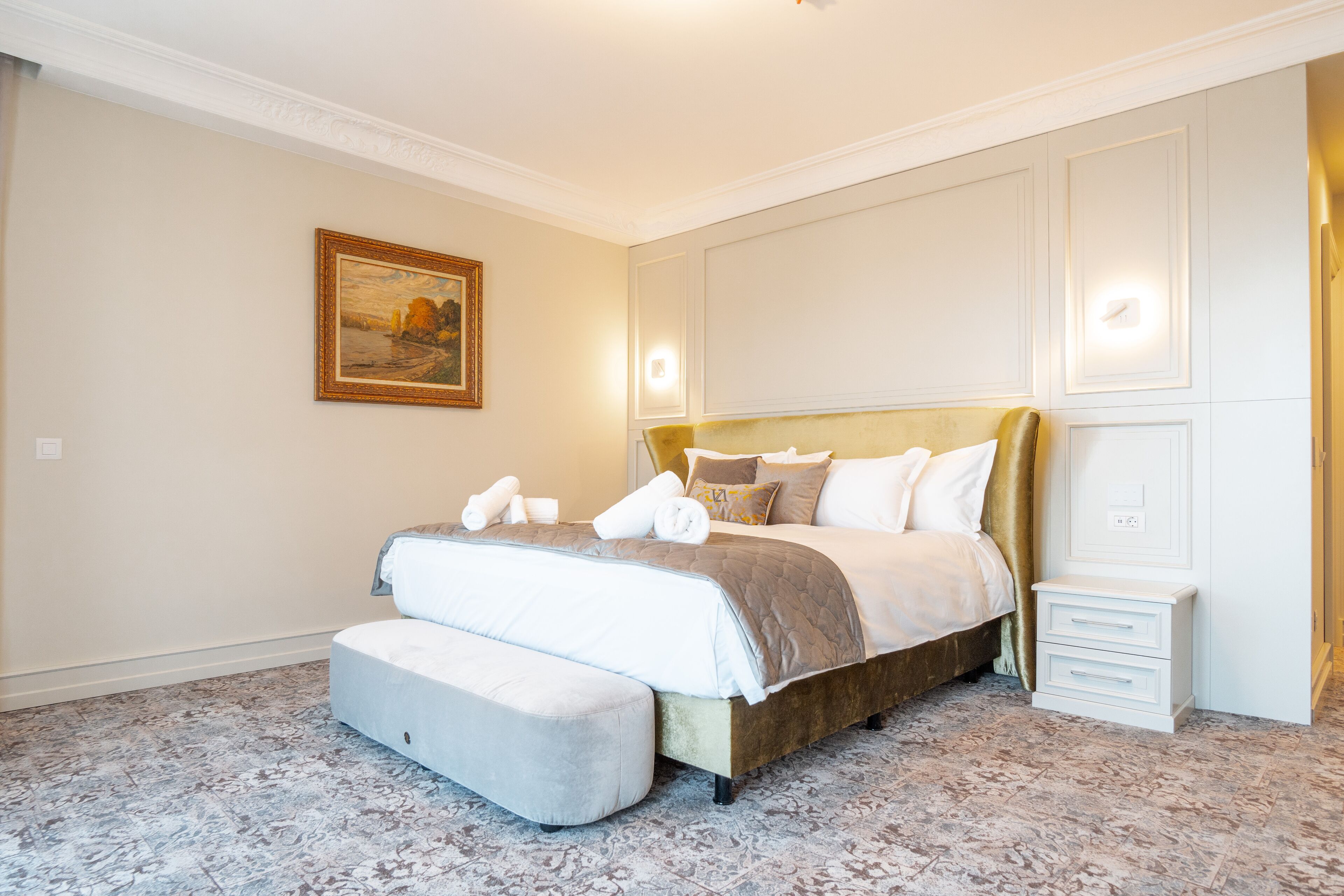 Une chambre bien rangée, avec un grand lit, une table de chevet et un tableau accroché au mur.