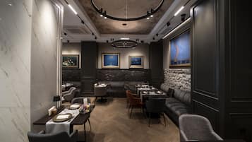 Un interno ristorante moderno con pareti in marmo, pavimento in legno e diverse tipologie di posti a sedere, tra cui tavoli e divani.