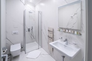 Un baño moderno con cabina de ducha de vidrio, un inodoro blanco, un lavamanos con espejo y una pared con diseño de mármol.