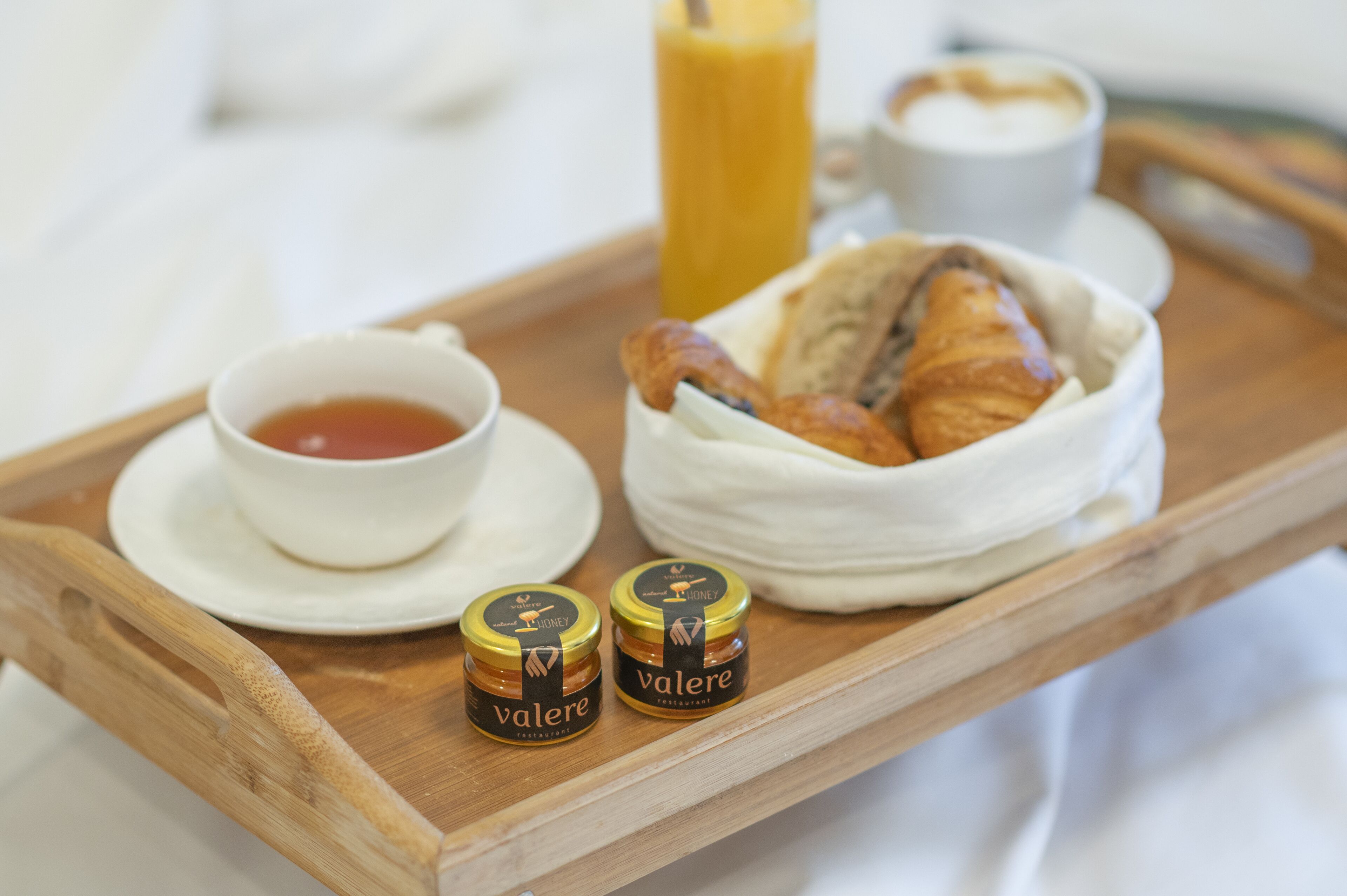 Bandeja de desayuno con cruasanes, frascos de miel, una taza de té y un vaso de zumo de naranja.