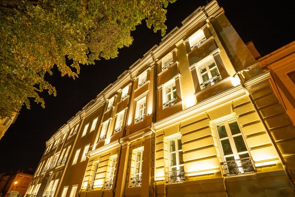 Un edificio de varios pisos con ventanas e balcones iluminados, que presenta detalles arquitectónicos clásicos.