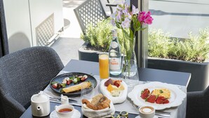 Una mesa de desayuno con platos de comida, una botella de agua, un vaso de jugo de naranja, una taza de té y un florero con flores.