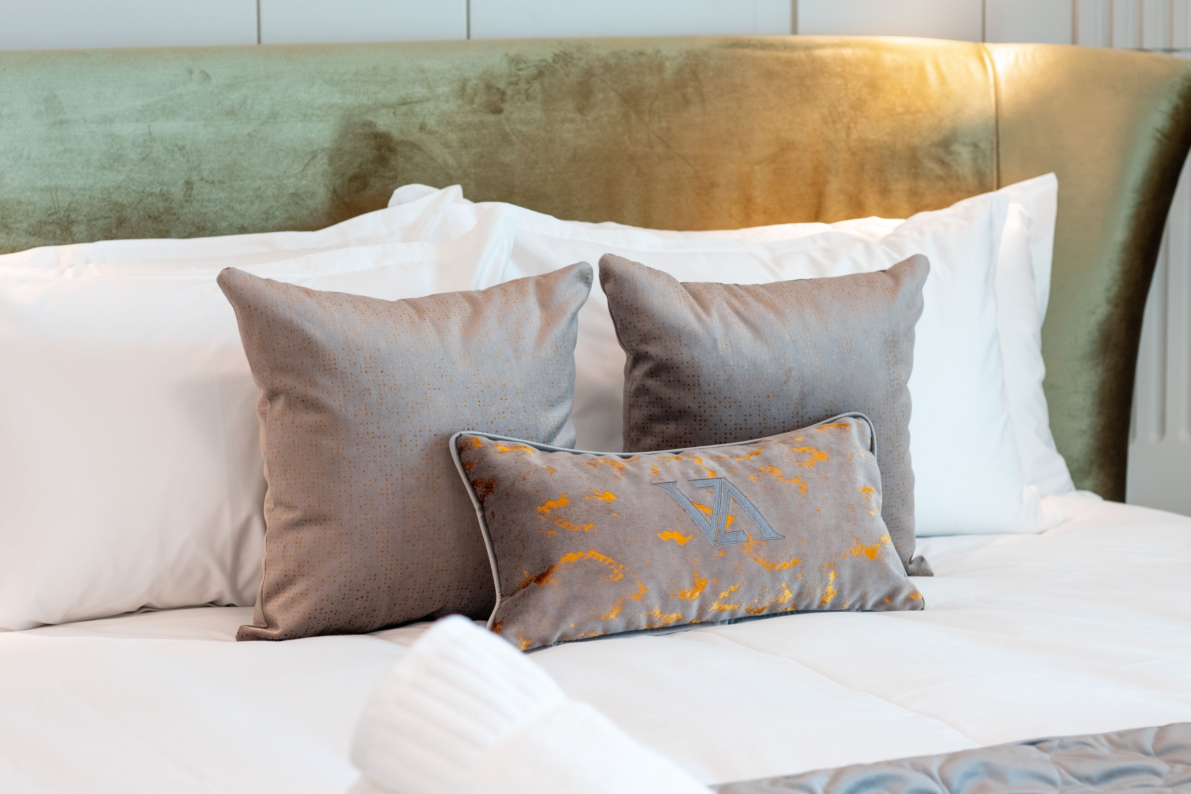 A bed with white and gray pillows, a green headboard, and a patterned bedspread.