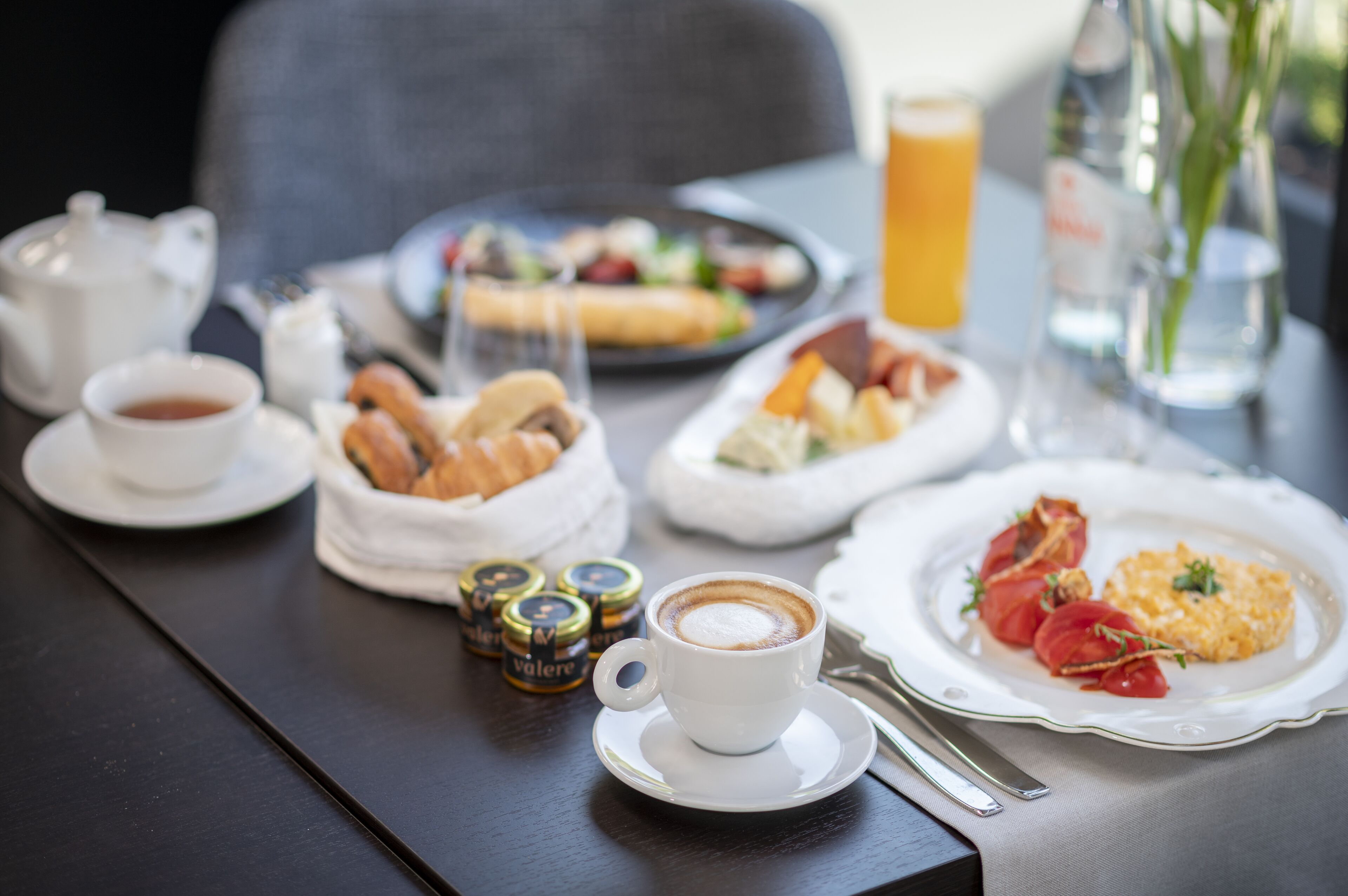 Une table mise pour le petit-déjeuner avec une tasse de café, des croissants et une assiette contenant des tomates et des œufs brouillés.