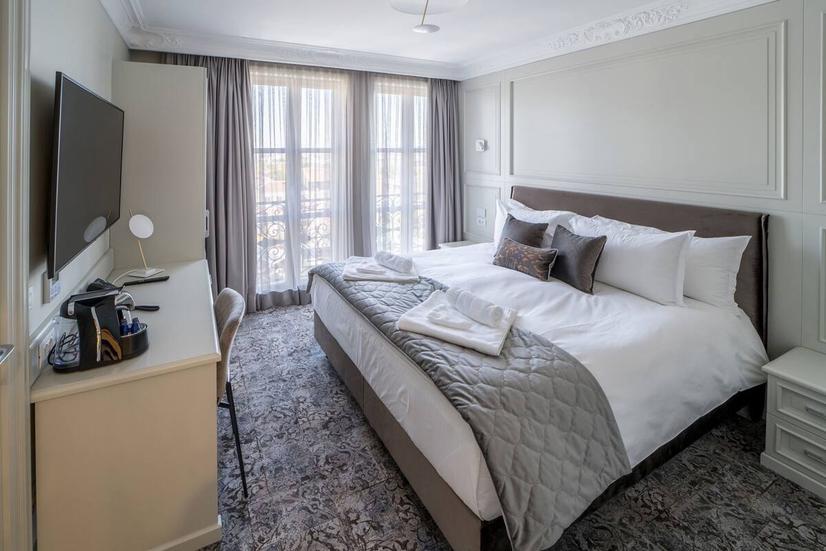 Quarto de hotel com cama, secretária, televisão e janela com cortinas.