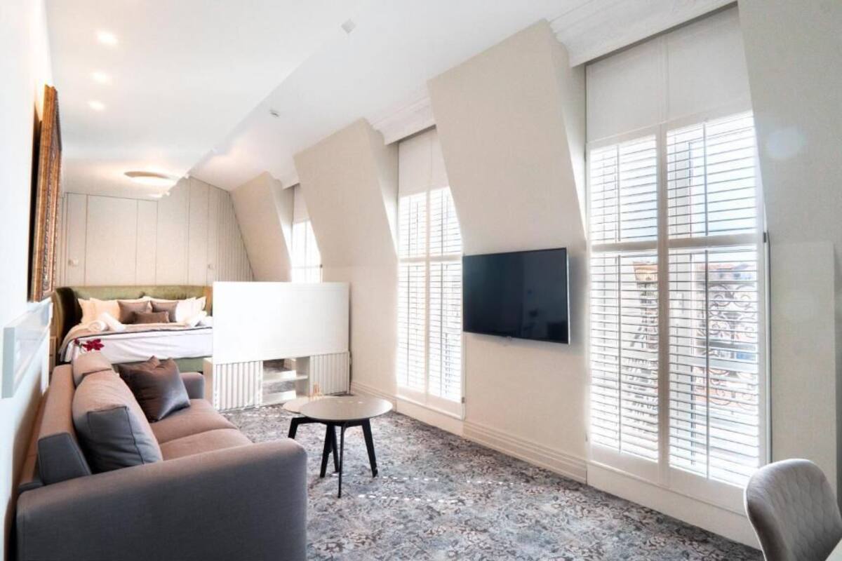 Quarto de hotel moderno com cama, sofá, televisão e janelas amplas.
