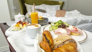 Bandeja de desayuno con cruasanes, queso, jamón y una taza de café sobre una cama de hotel.