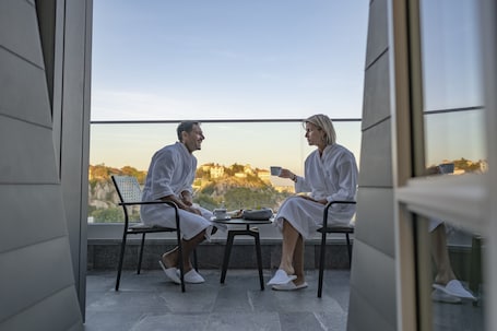 Two people sitting at a table on a balcony with a view of a cityscape.