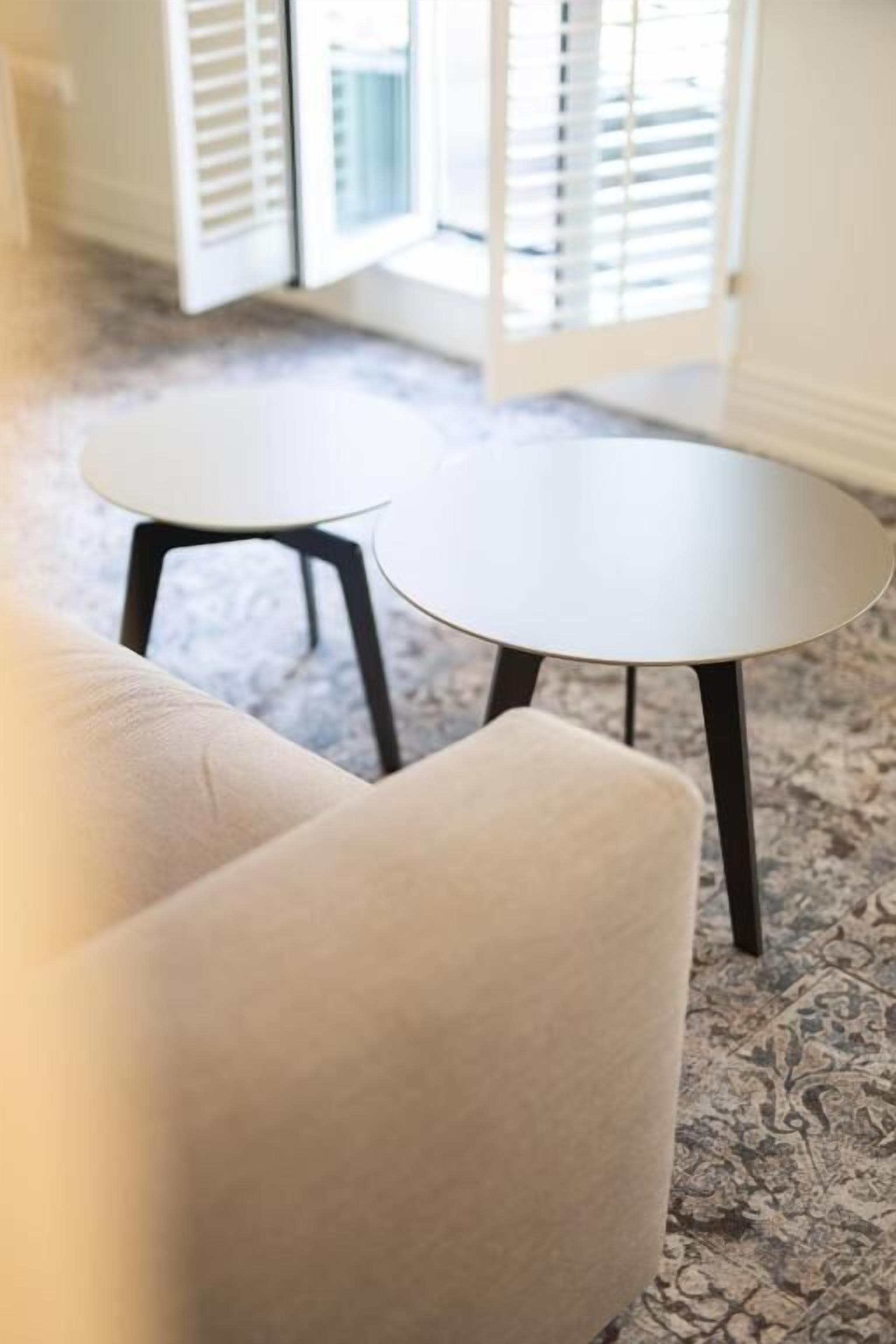 Ein Zimmer mit einem beigefarbenen Sofa und zwei kleinen, runden Tischen mit schwarzen Beinen.