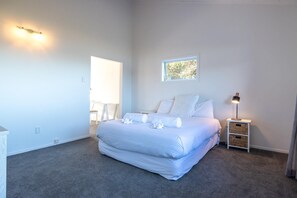 A bedroom with a large bed, a bedside table with a lamp, a small window, and a door.