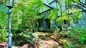 A stone building with a brick pathway leading to it, surrounded by lush greenery. - IPPUKAKU (Tsumagoi)