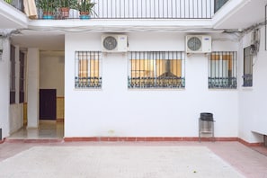 Une cour avec des murs blancs, des fenêtres grillagées et deux unités de climatisation.