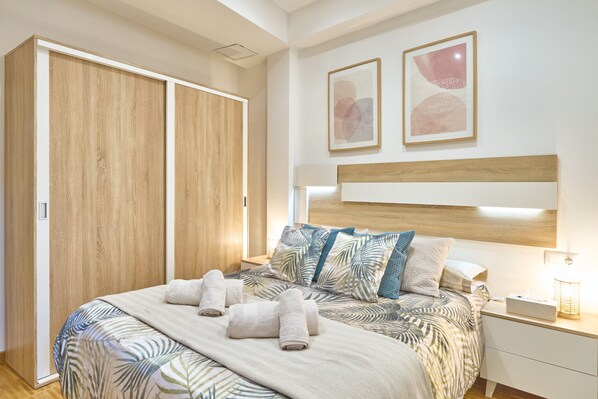 Une chambre à coucher comprenant un lit, une table de chevet, une commode, une armoire et deux tableaux encadrés accrochés au mur.