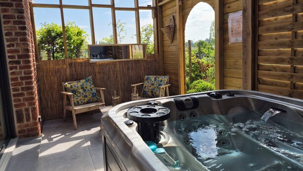 A hot tub in a wooden room with a view of greenery outside. - Suites Spa Détente de la lys (La Gorgue)