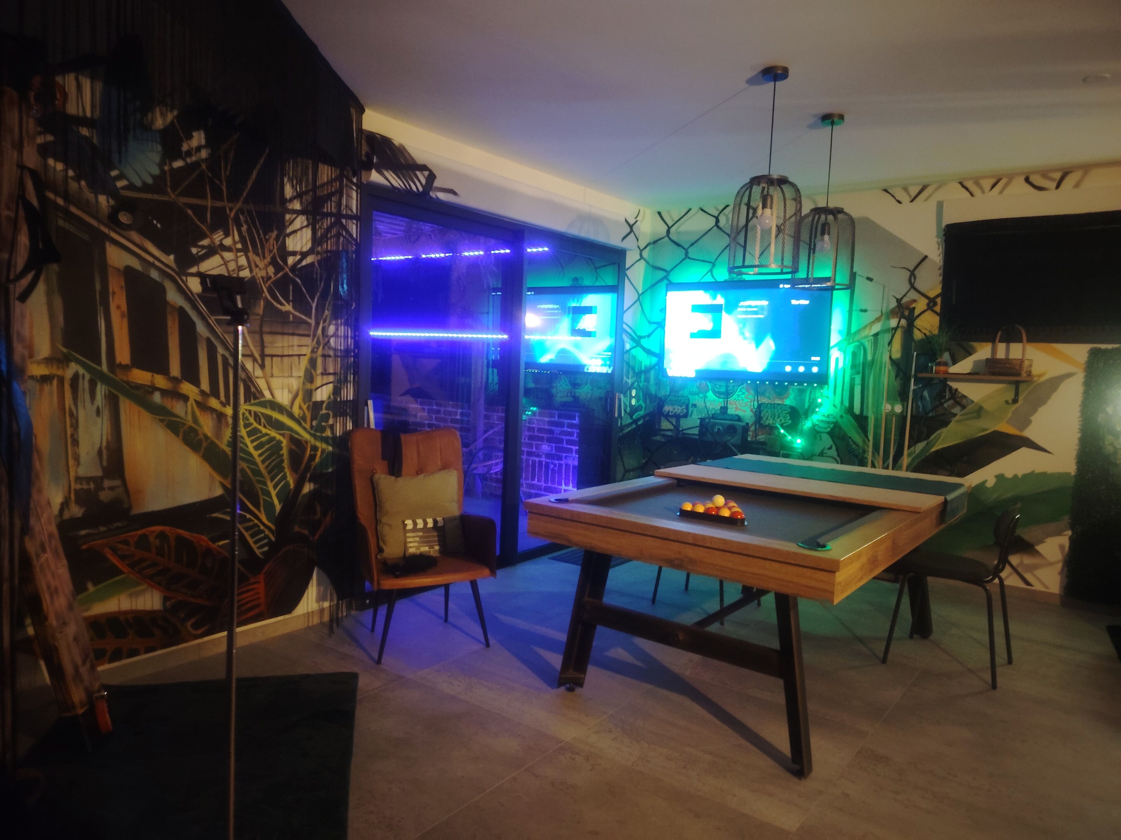A billiards table in a room with a mural and LED lighting.