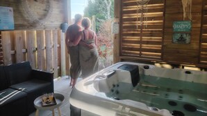 A wooden cabin interior with a hot tub, a couch, and a sign indicating a happy place. - Suites Spa Détente de la lys (La Gorgue)