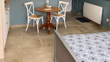 A compact room with a bed, a small round table with chairs, a wall clock, and a radiator.