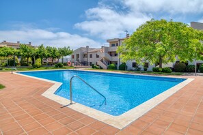 Une piscine dotée d’une terrasse carrelée, entourée d’immeubles avec balcons et d’arbres.