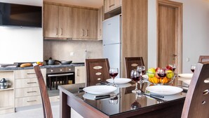 A modern kitchen with wooden cabinets, a refrigerator, and a dining area with a glass table set for two. - Apartment Deluxe Suite with Sea View B close to Beach with Shared Pool & Wi-Fi (?e???da)