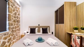 Habitación de hotel con pared de piedra, cama con cabecera, armario de madera y escritorio con una planta.