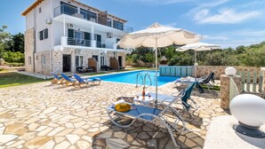 Uma casa de dois andares com piscina, área de estar externa e um pátio de pedra.